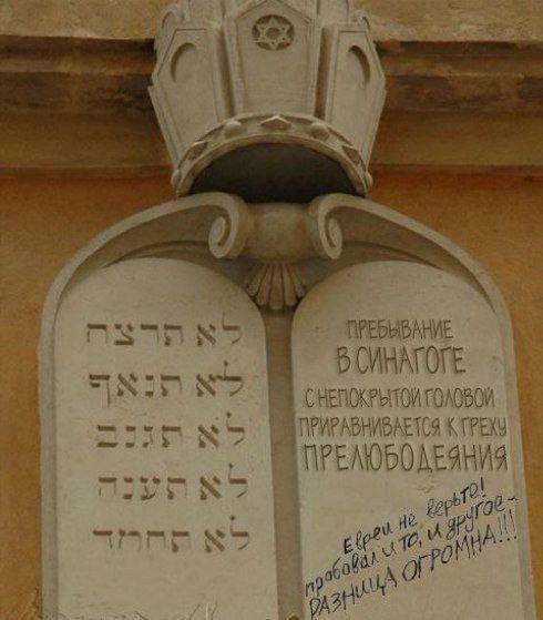 На каменных скрижалях выгравированы заповеди на иврите. Рядом текст: «Пребывание в синагоге с непокрытой головой приравнивается к греху прелюбодеяния». Ниже приписка от руки: «Евреи, не верьте! Пробовал и то, и другое – разница огромна!!!»