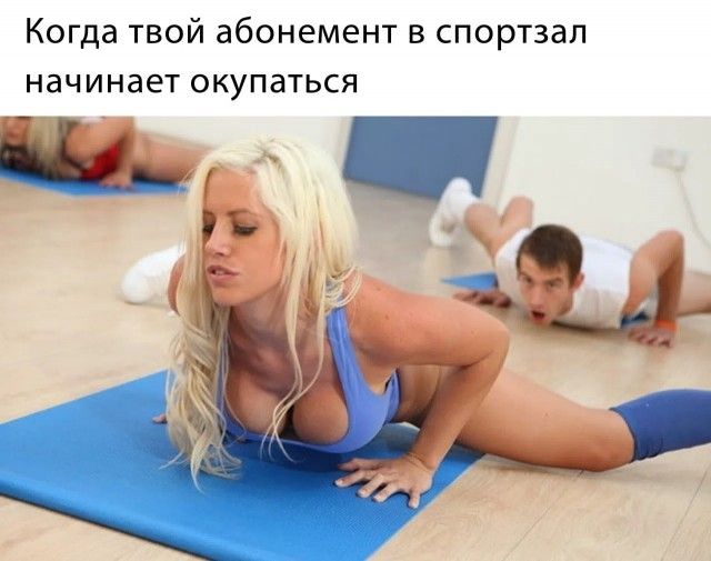 Когда твой абонемент в спортзал начинает окупаться. Женщина в спортивном топе делает упражнение на коврике, мужчина на заднем плане удивленно смотрит на нее.