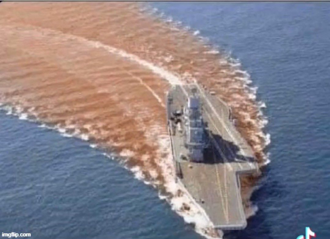 Военный корабль идёт по морю, оставляя широкий коричневый след от воды.