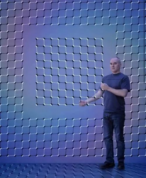 Человек в темной футболке стоит внутри большого сетчатого лабиринта из квадратных полей.