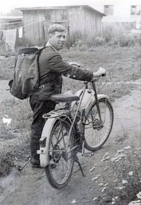 Человек с рюкзаком возле старого мотоцикла на сельской улице