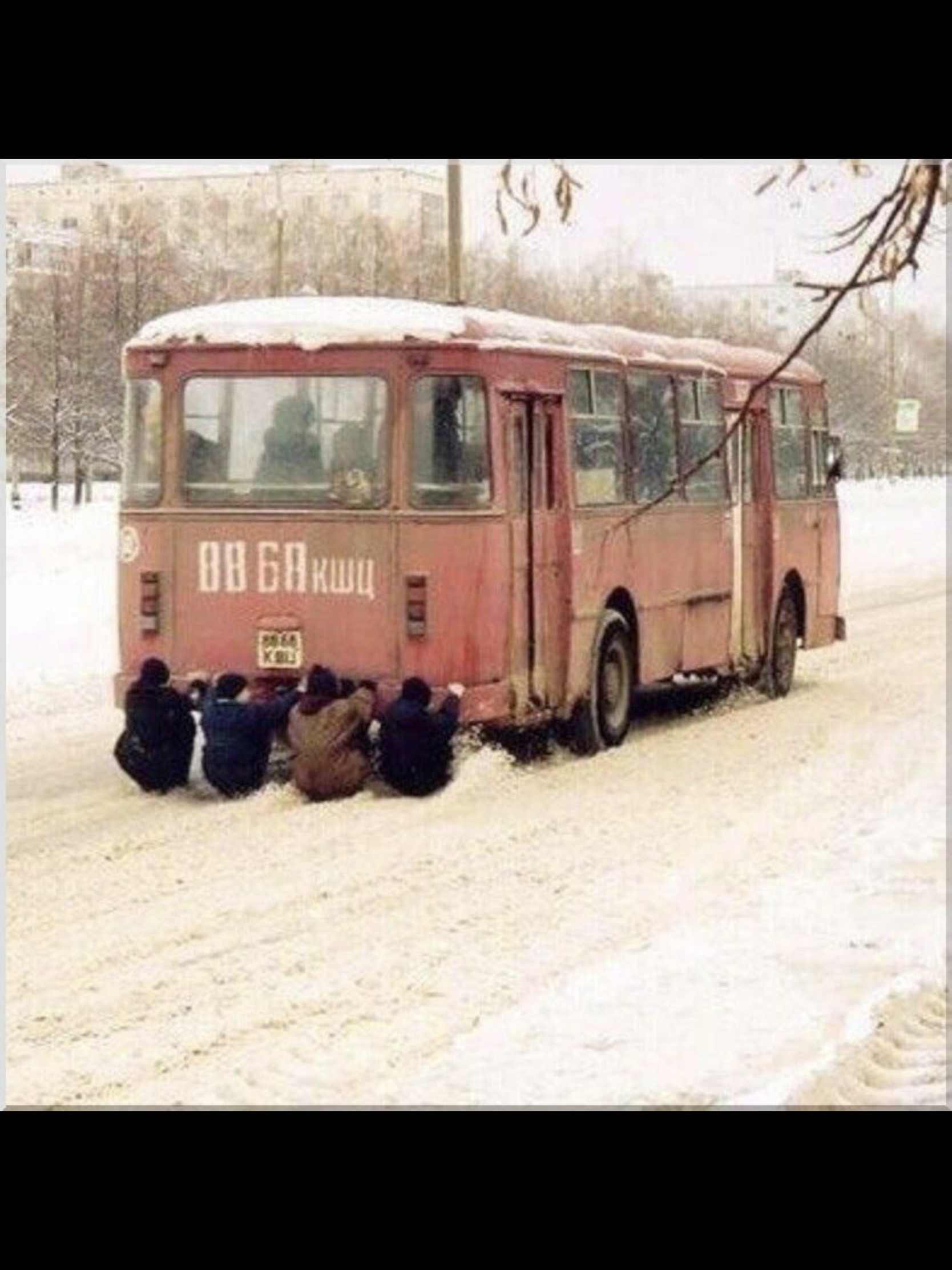 Старый автобус застрял в снегу, группа людей пытается толкнуть его.