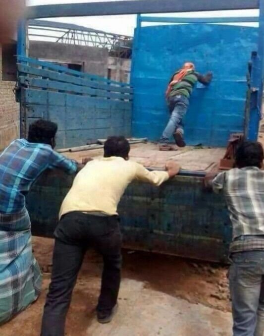 Человек взбирается по бортовой стенке грузовика, спину держат трое людей снизу.