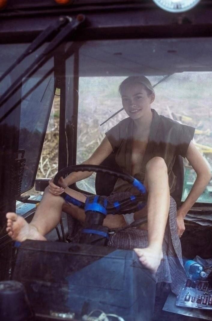 В кабине грузового автомобиля девушка улыбается, сидит на водительском месте, ноги на руле.