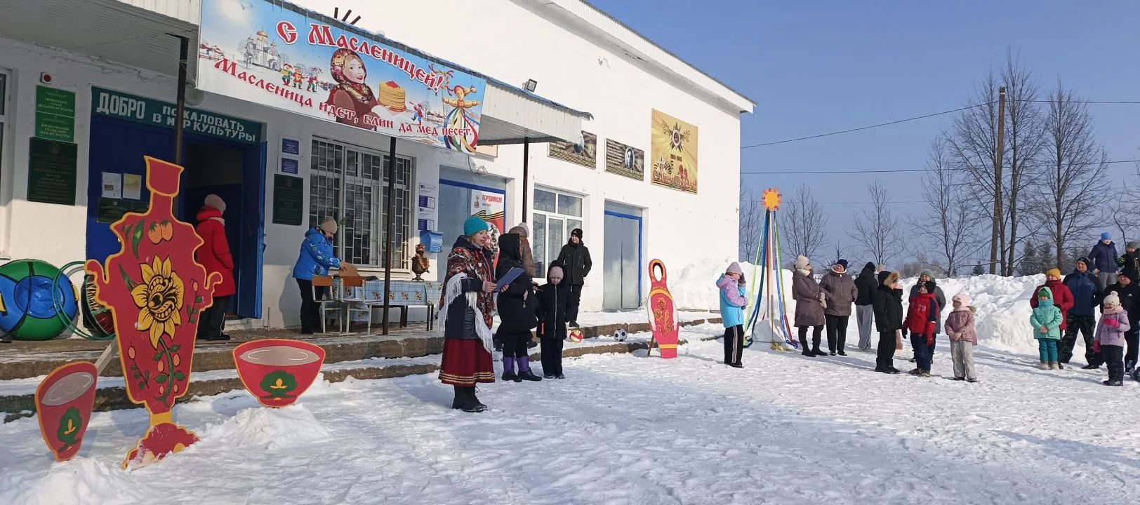 Зимняя улица у здания, люди в костюмах и яркие фигуры для праздника.