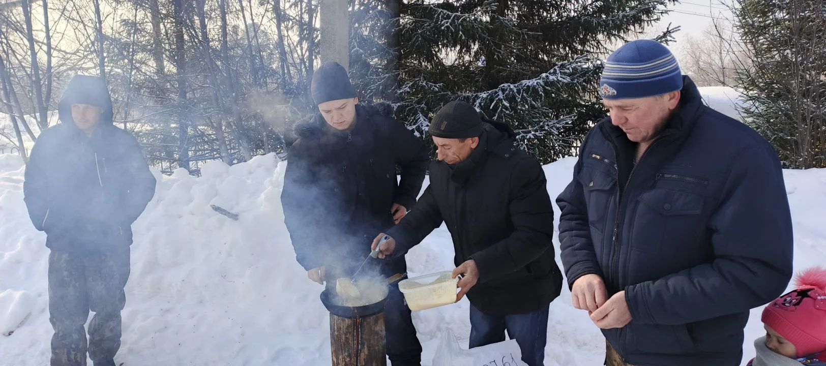 Группа мужчин на улице в зимнем лесу жарит что-то над костром.