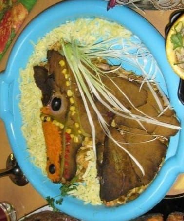 Блюдо на тарелке: голова животного из мяса на рисе с зеленью