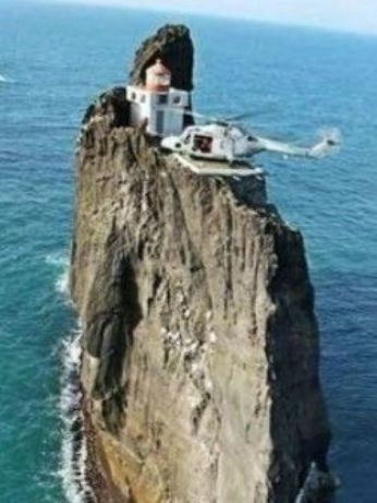 Уединённая скала в море с домиком и вертолётом на вершине.