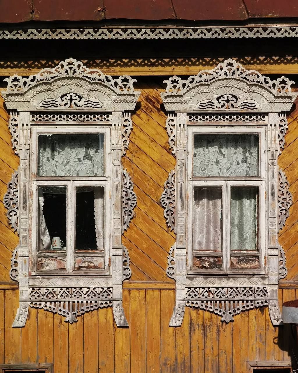 Два старинных резных окна на желто-оранневой деревянной стене