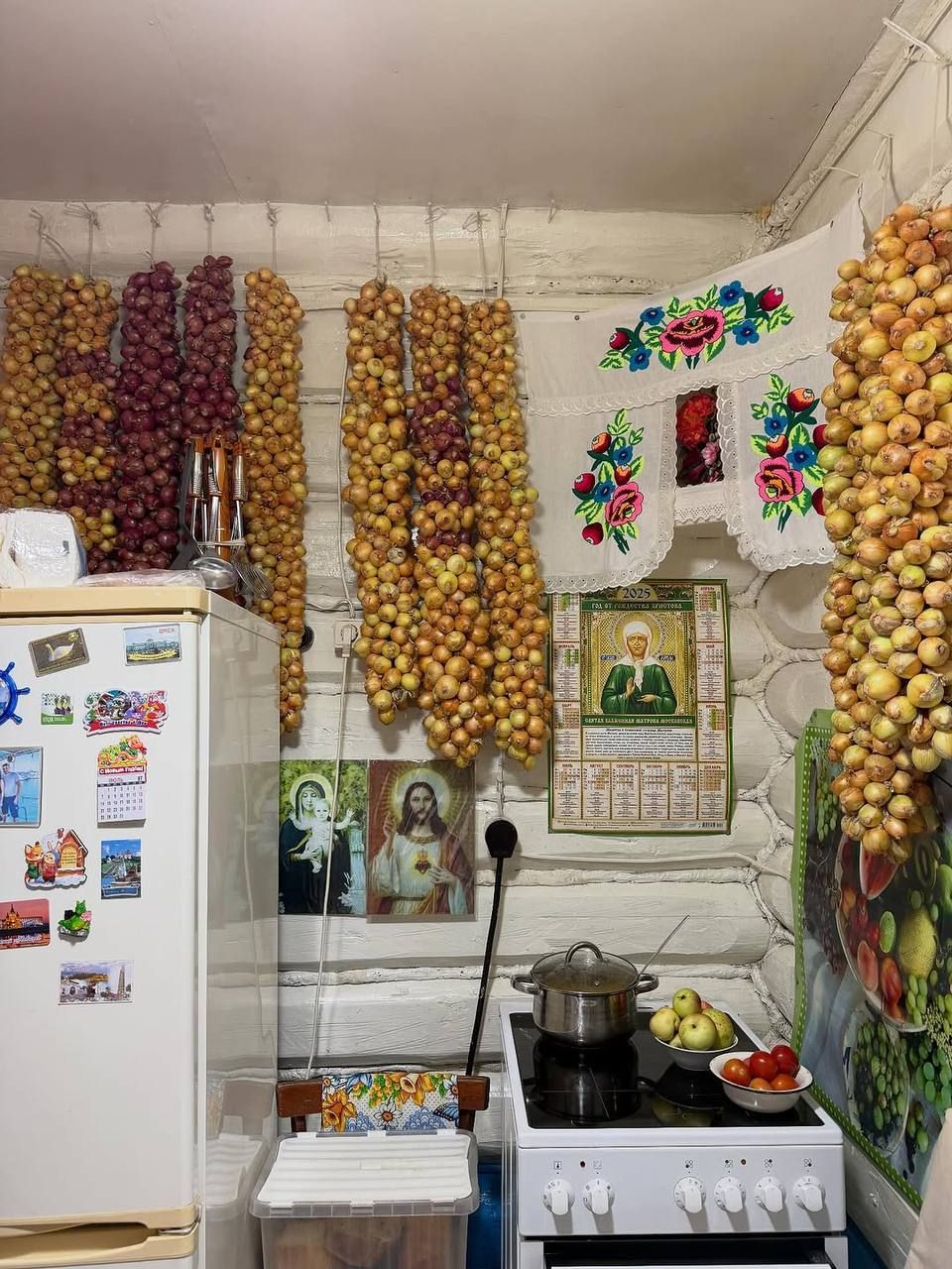 Кухня с гирляндой лука, рушниками на стене и бытовыми предметами.