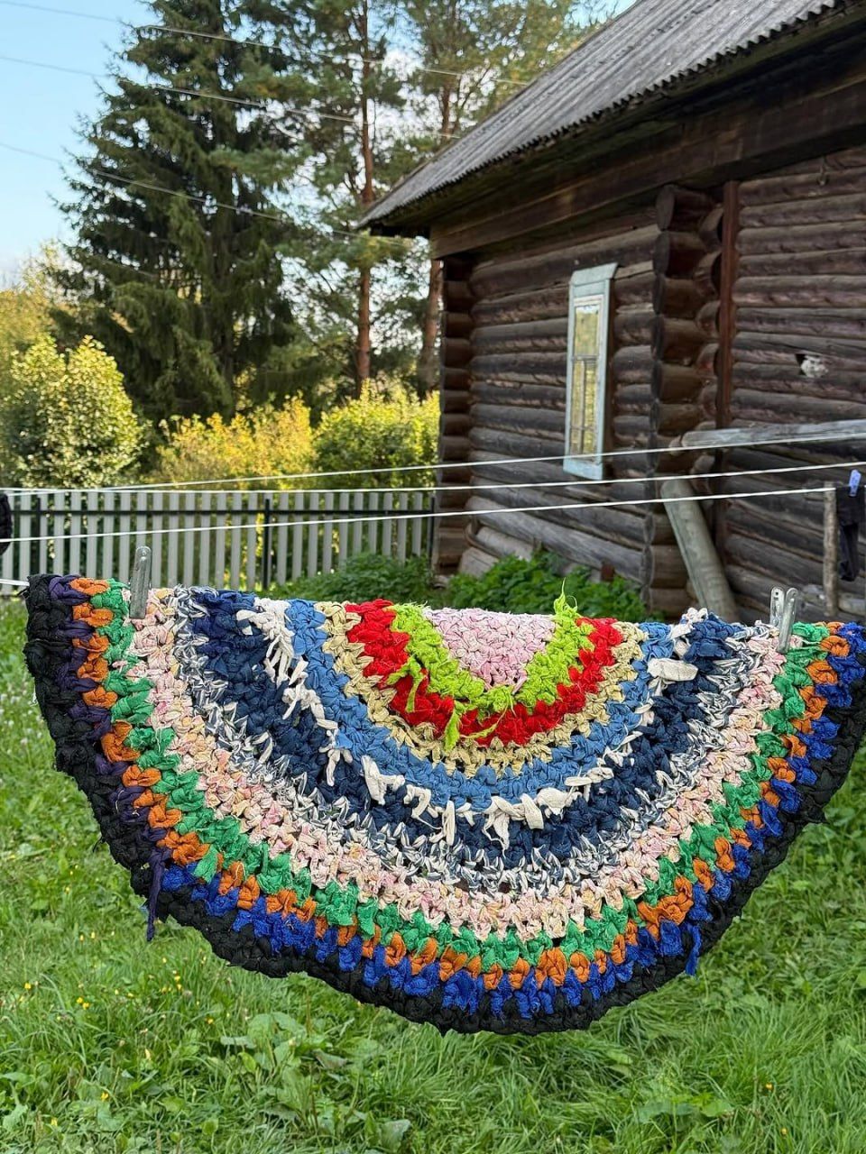 Красочная вязаная крючком вещь, развешанная на верёвке перед деревянным домик