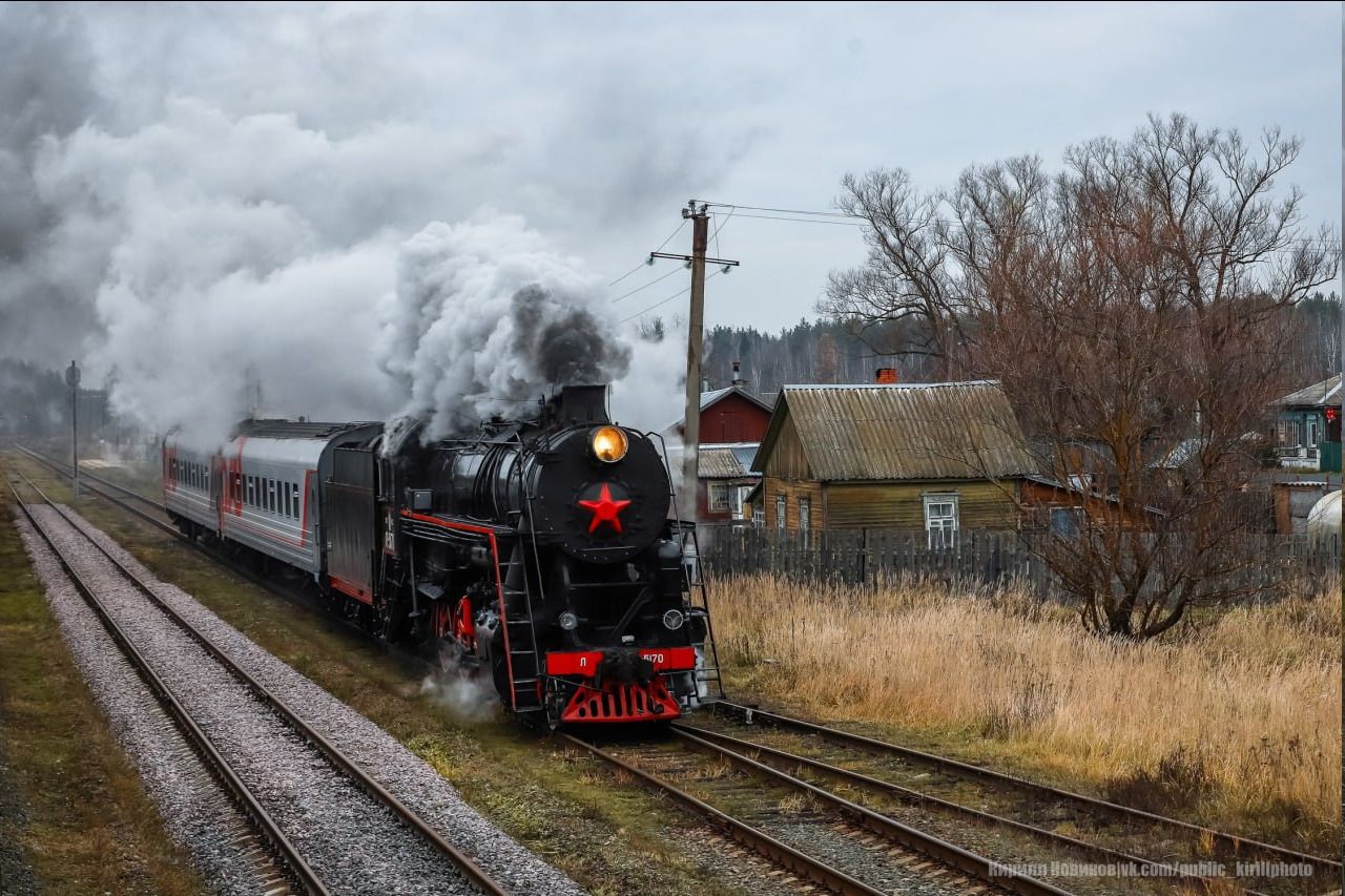 Паровоз на рельсах с красной звездой в деревенском пейзаже.