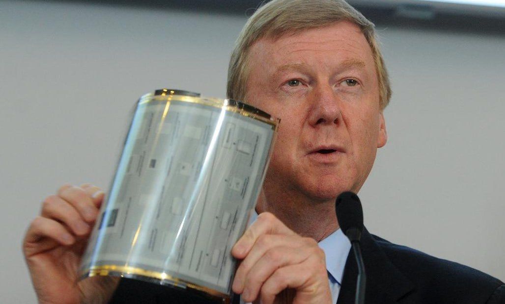 Мужчина держит металлическую банку или цилиндр на фоне пресс-конференции.