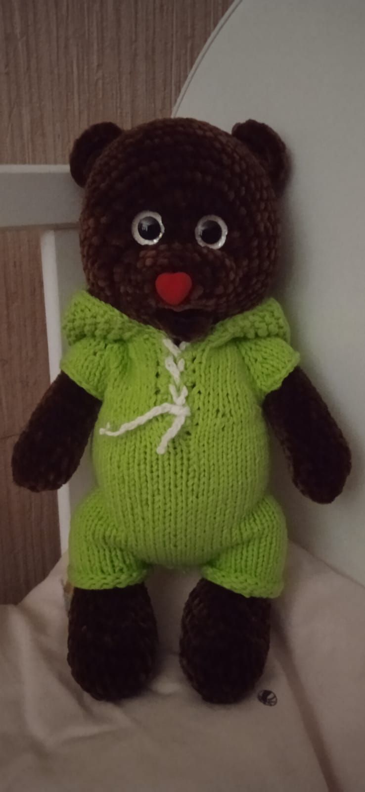 Коричневая меховая игрушка-ведмедик в ярко-зеленом комбинезоне.
