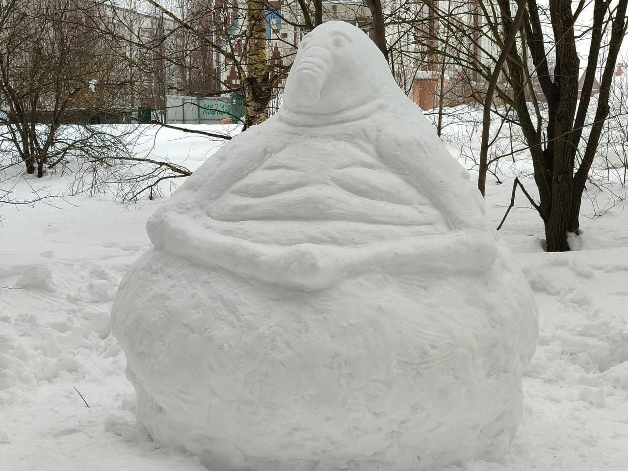 Снеговая скульптура в виде круглого пузыря с лицом на улице зимой.