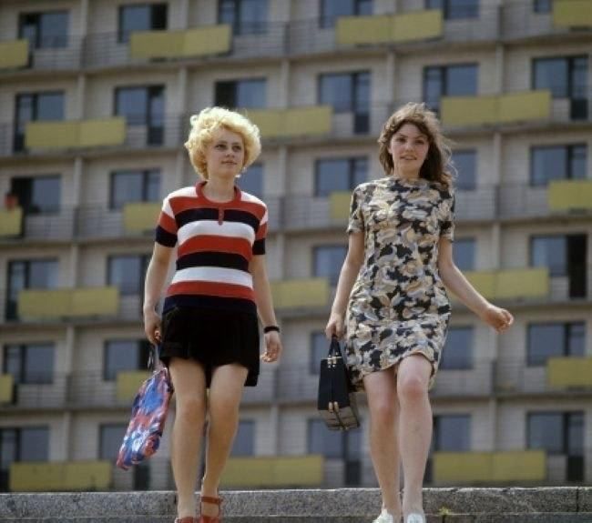 Две женщины в модных нарядах идут по лестнице на фоне жилого дома.