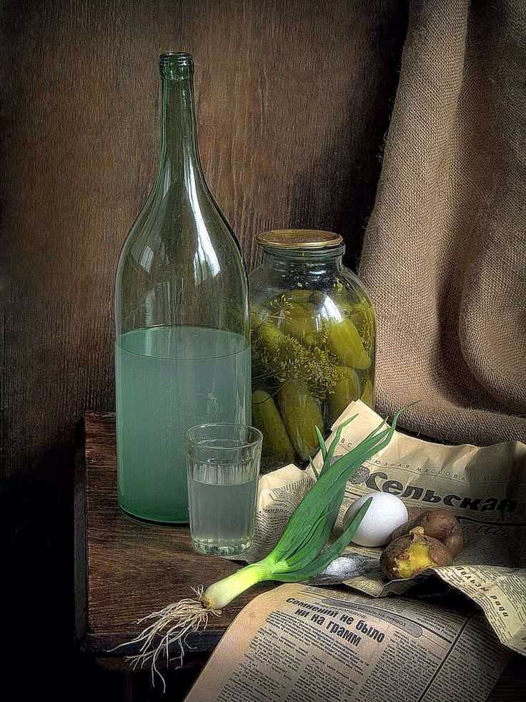 Бутылка с жидкостью, банка с маринованными овощами, лук, чеснок, яйцо и газета на темном фоне.