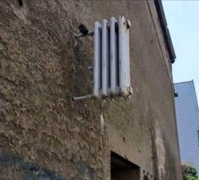 Старая кирпичная стена, радиатор, на котором сидит черный кот.