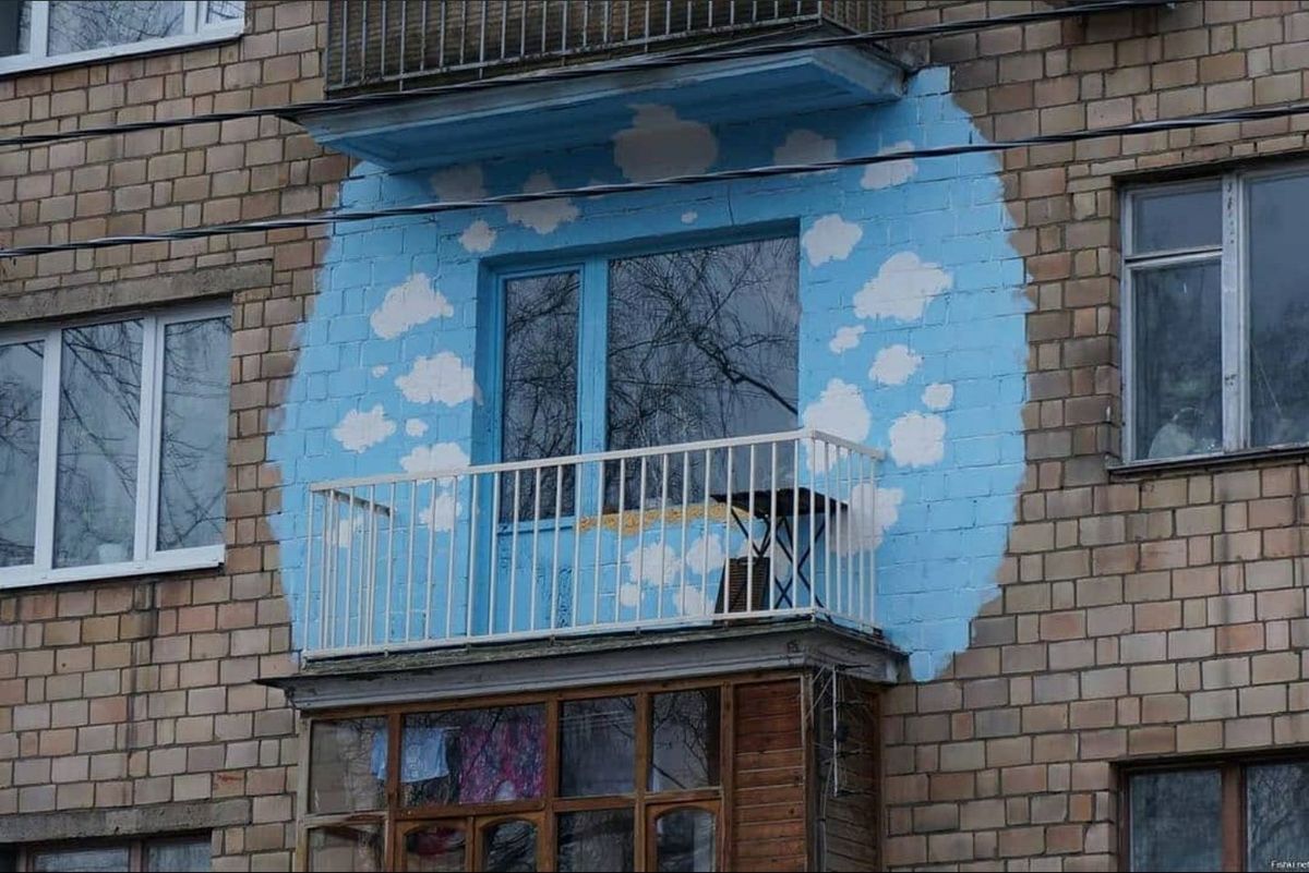Балкон на кирпичном доме оформлен рисунком неба с облаками вокруг окна.