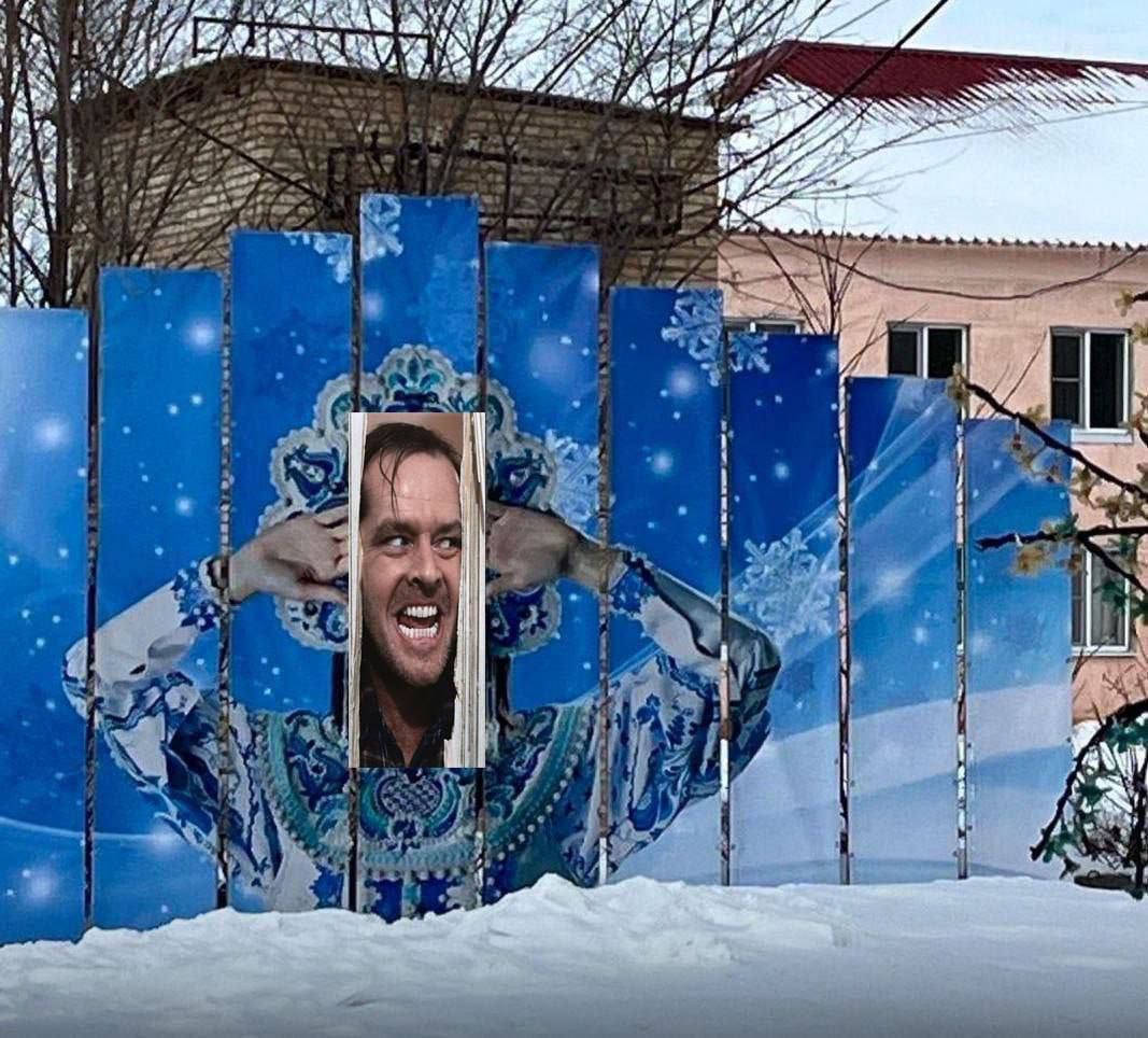 Человек выглядывает через прорезь в декоративной синей стене с орнаментом.