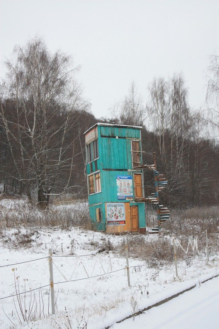 Заснеженная деревянная башня с внешней лестницей посреди поля.