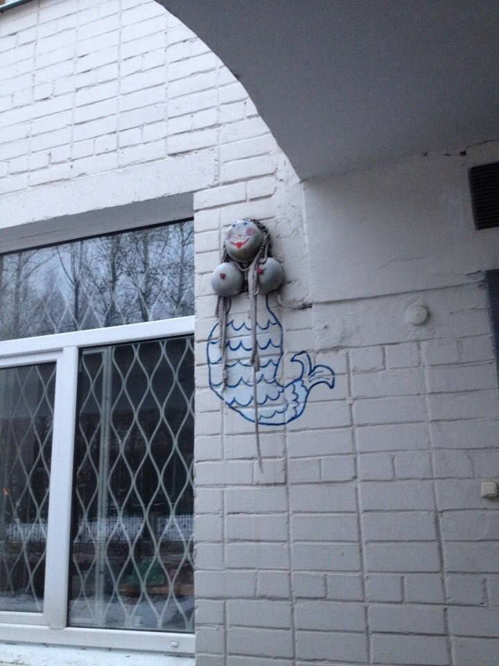 Уличная графика на белой кирпичной стене в виде птицы с воздушными шарами/колпачками сверху