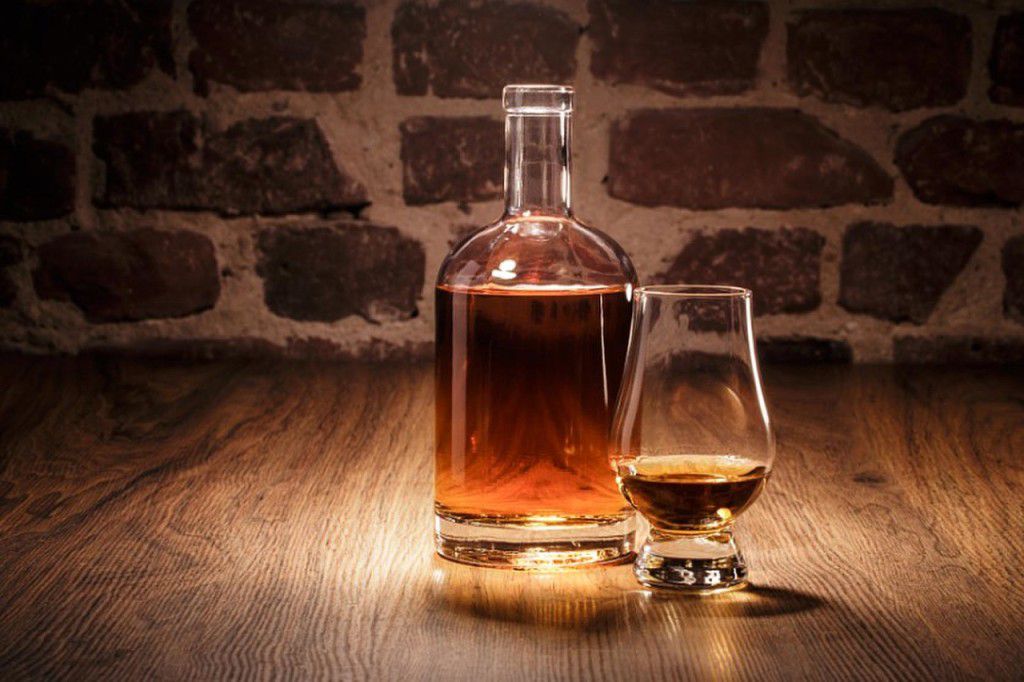 Бутылка и бокал с алкоголем на деревянном столе у кирпичной стены