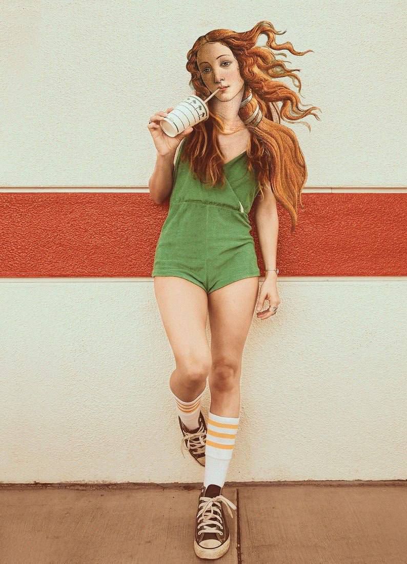 Молодая женщина в зелёном комбинезоне стоит у стены и пьёт напиток через трубочку.