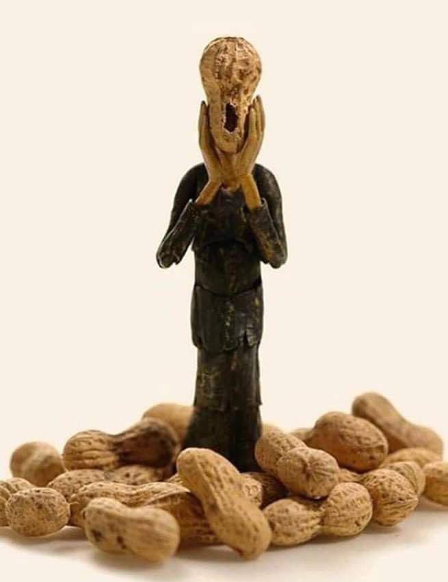 Статуэтка в черном наряде держит орех над головой, вокруг рассыпаны арахисы.