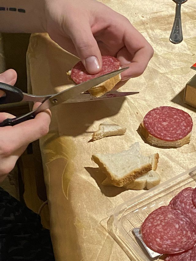 Человек режет салями ломтики поверх хлеба на столе