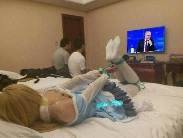 Человек лежит на кровати в комнате, ноги подняты вверх в носках; в телевизоре мужчина, сидящие рядом люди смотрят.