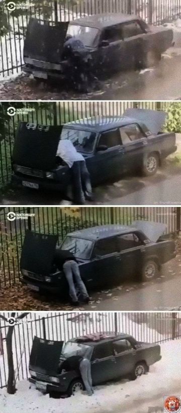 Человек пытается открыть капот у застрявшей в снегу машины возле забора.