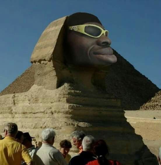 Сфинкс с человеческим лицом в очках и толпой туристов у подножия.