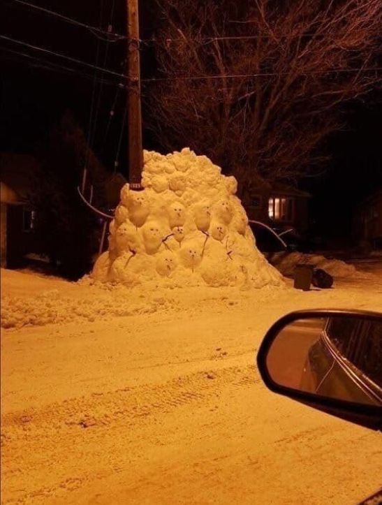 Снежная куча, оформленная как группа снежных человечков на улице ночью.