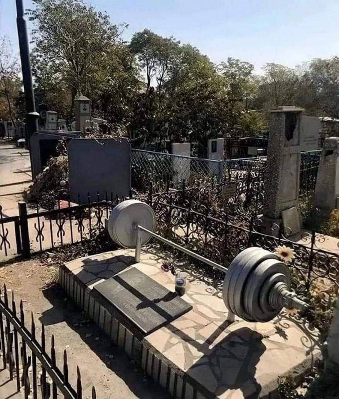 Гробница на кладбище с штангой и дисками, лежащая на надгробии.