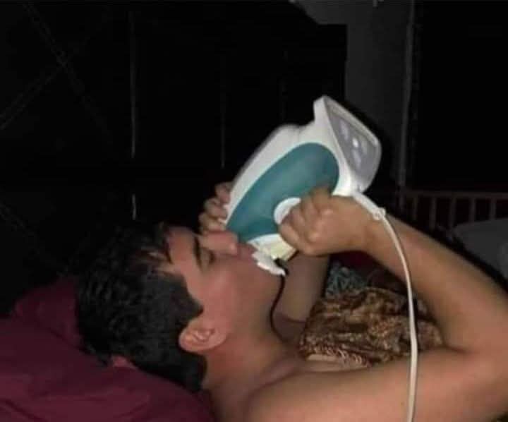 Мужчина лежит в кровати и держит утюг во рту