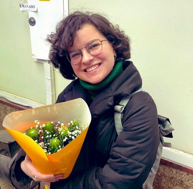 Женщина на улице с букетом ярких цветов, улыбается.