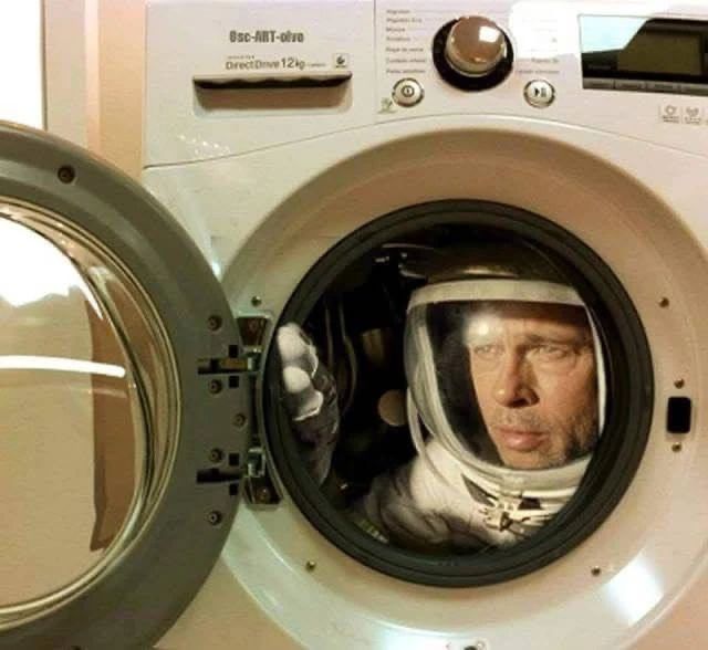 Человек в космическом скафандре выглядывает из дверцы стиральной машины, создавая комичный образ