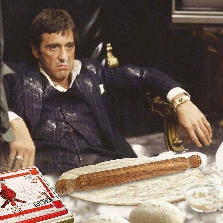 Серый мужчина в костюме сидит за столом, перед ним развёрнутый рулон теста/пальца и карты на столе