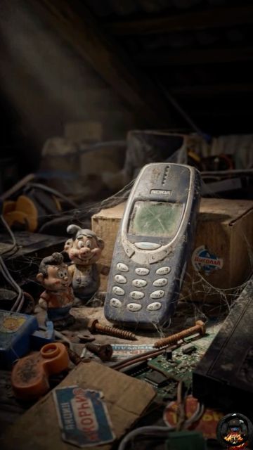 Nokia на кнопочном телефоне; на фото видны пыль и паутина вокруг старого устройства, коробки и мелкие фигушки. На некоторых наклейках можно разобрать буквы Cyrillic: Код.