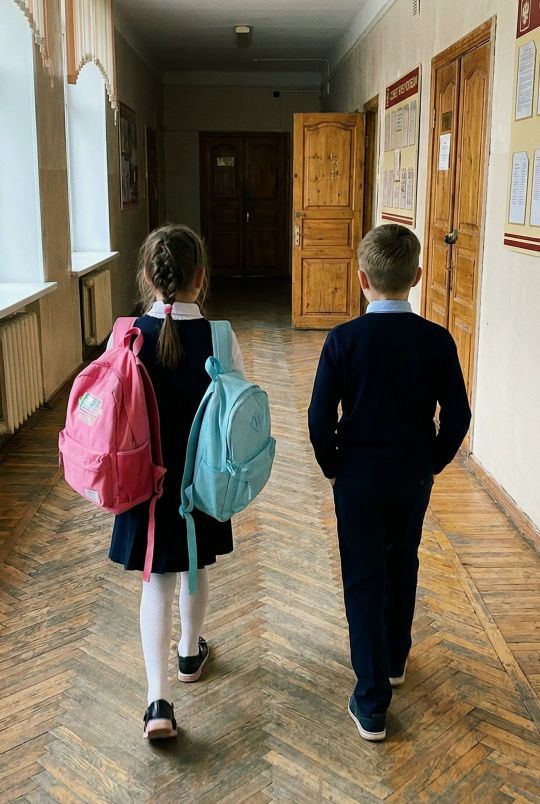 Две школьника идут по длинному коридору со школьными рюкзаками.