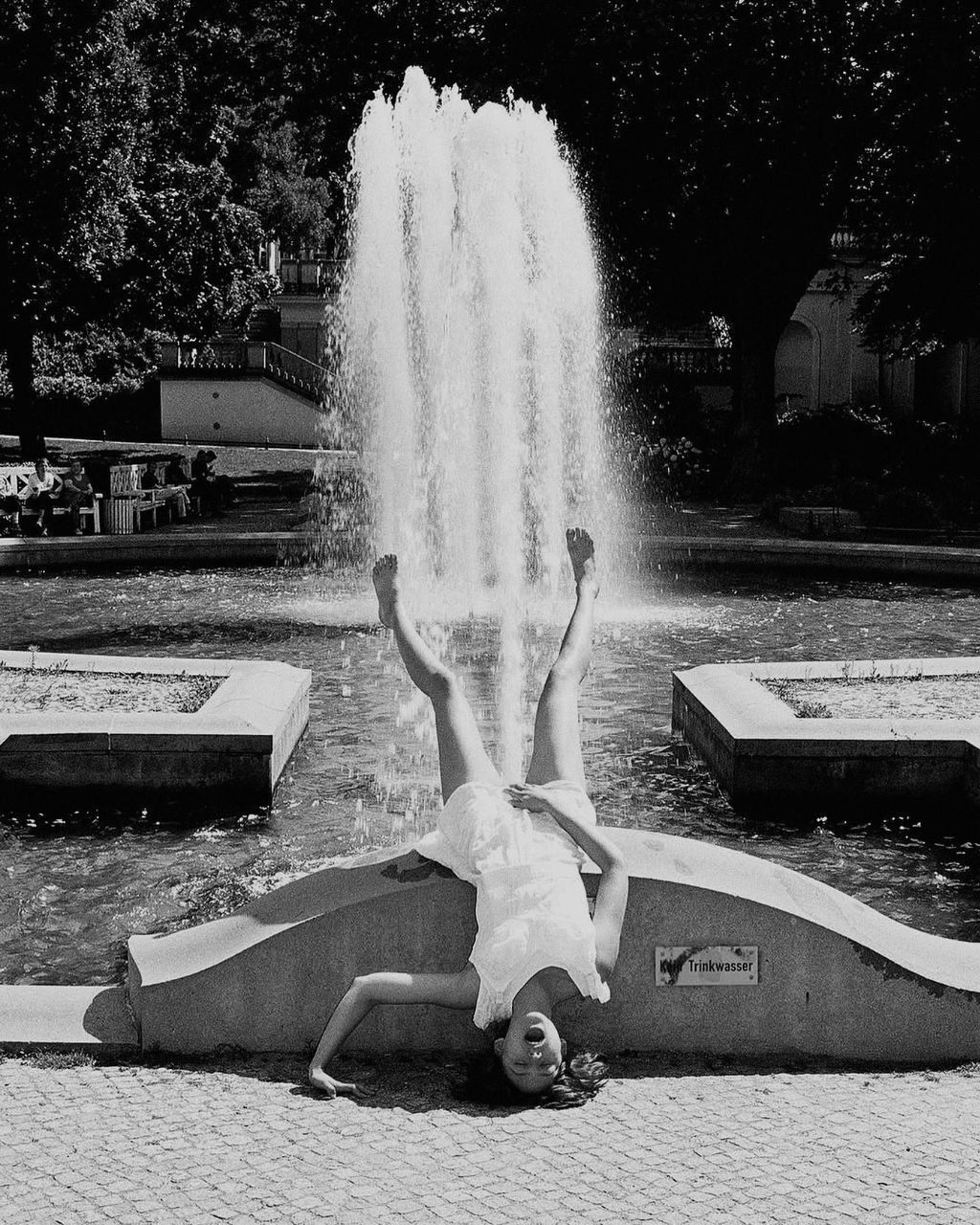 Черно-белое фото ребёнка у фонтана, он делает стойку головой/руками на скульптуре у водяной струи