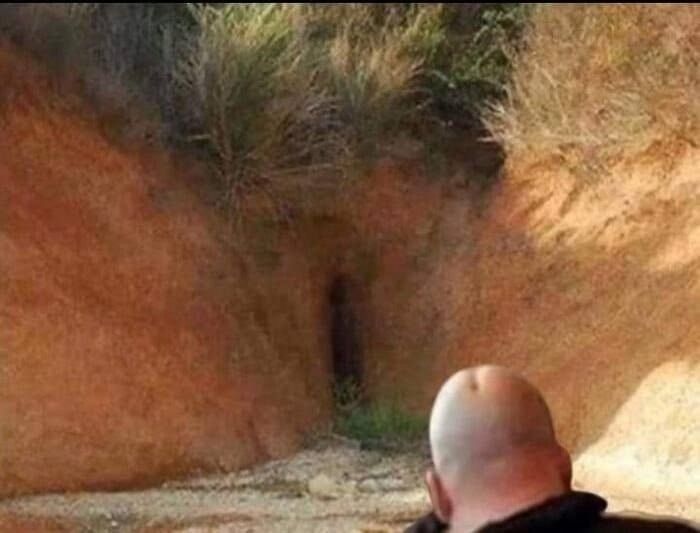 Человек стоит лицом к узкой норе между скалами в пустынной местности.