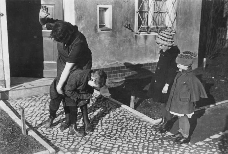 Черно-белая сцена на улице: взрослый мужчина держит за плечо мальчика, рядом идут двое детей.