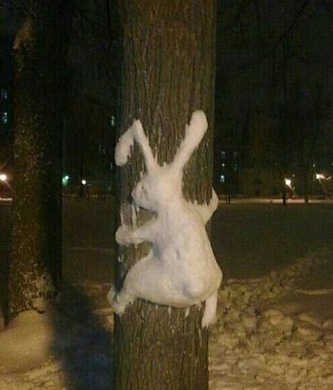 Снеговая фигура зайца, обвязанная вокруг ствола дерева ночью.