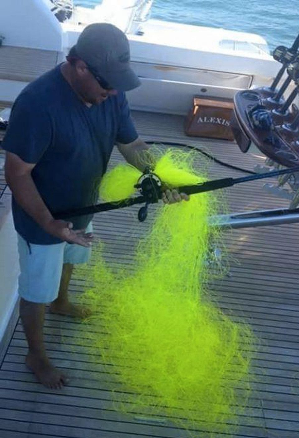 Мужчина на катере держит рыболовную снасть с ярко-жёлтой неоново-жёлтой сеткой/леской.