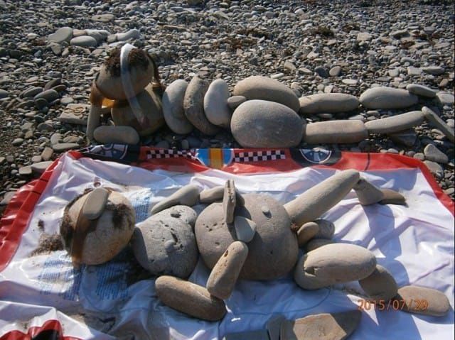 На пляже каменные фигуры и собака рядом, всё лежит на ткани под камнями.