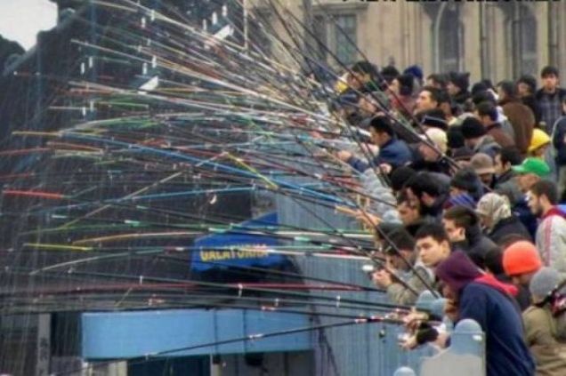 Толпа людей на улице, протягивает множество длинных палочек/фонариков в одну сторону.