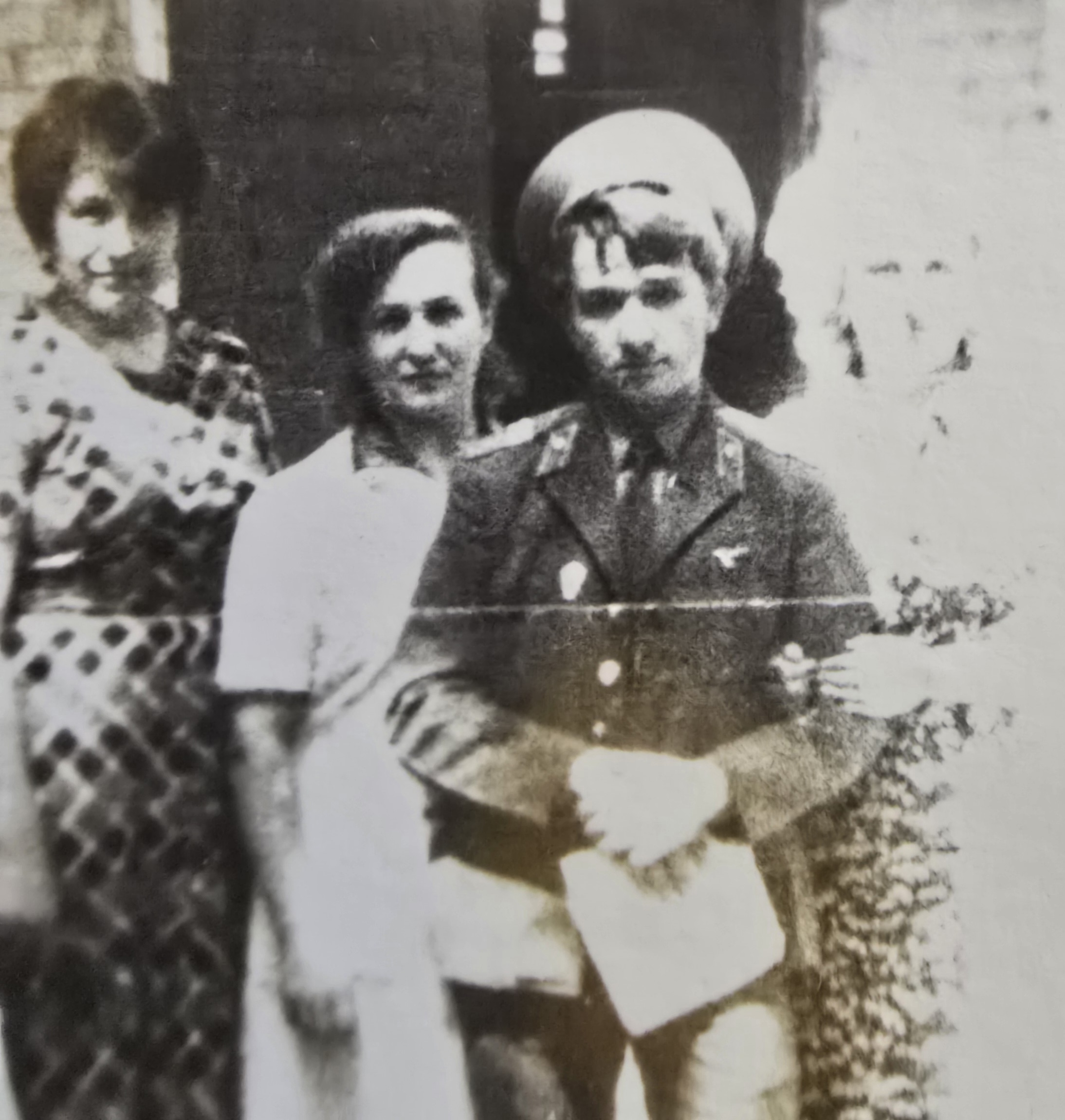 Старая черно-белая фотография: мужчина в военной форме и кепке стоит рядом с двумя женщинами.