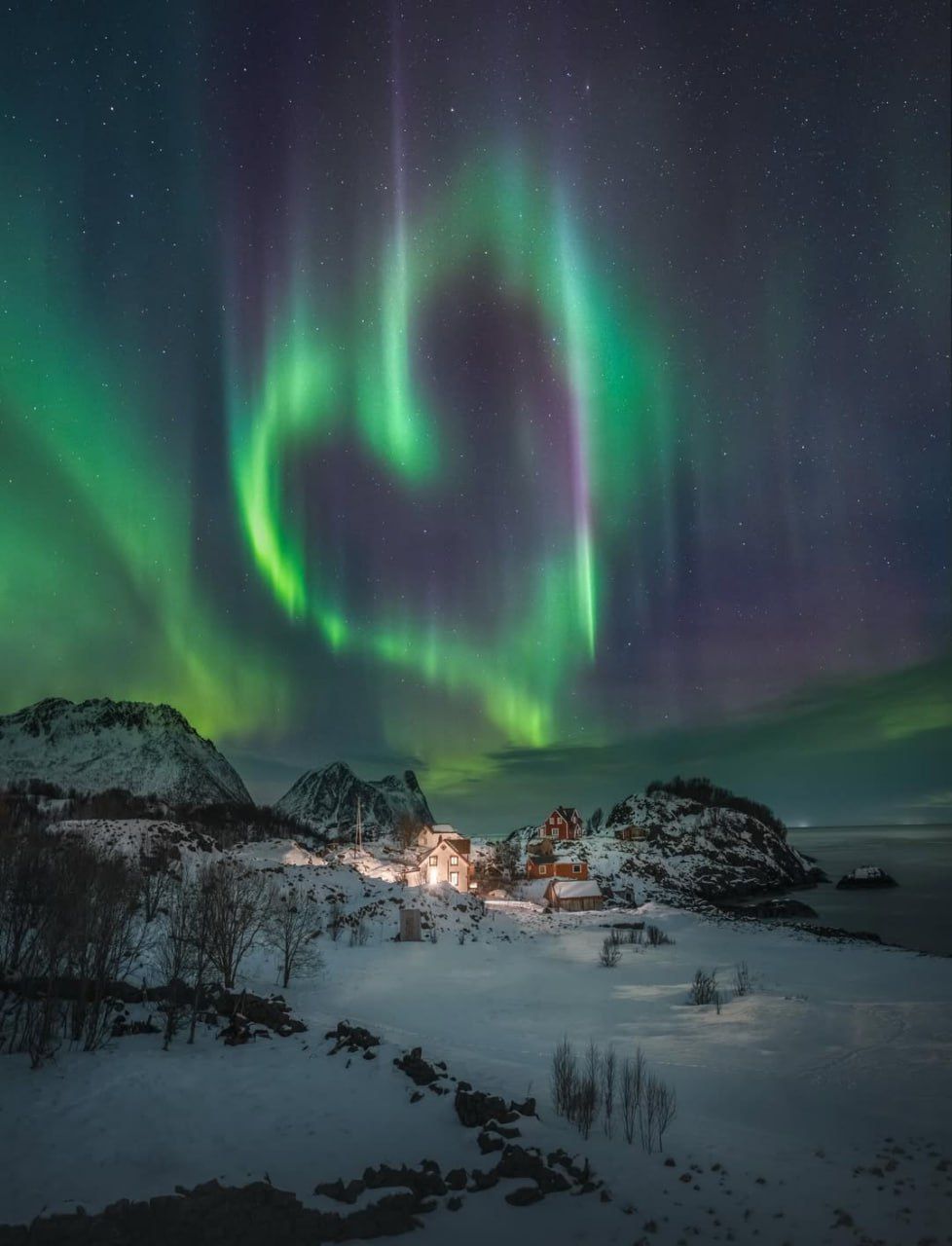 Северное сияние над заснеженной деревней у моря.
